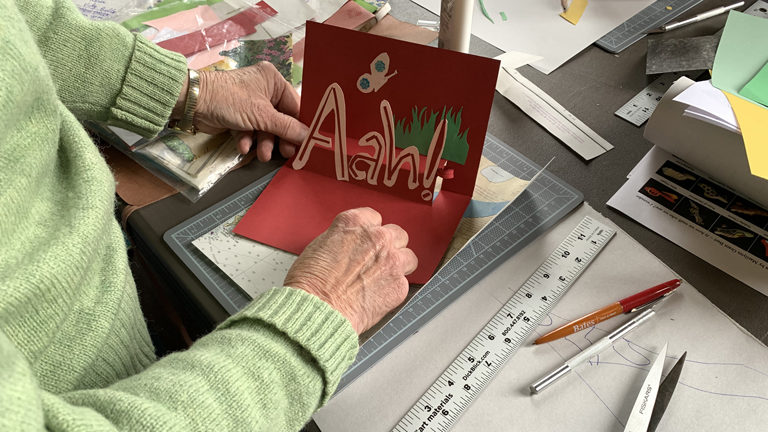 A program participant's art project, a card that says "Aah!" with a picture of a butterfly and grass