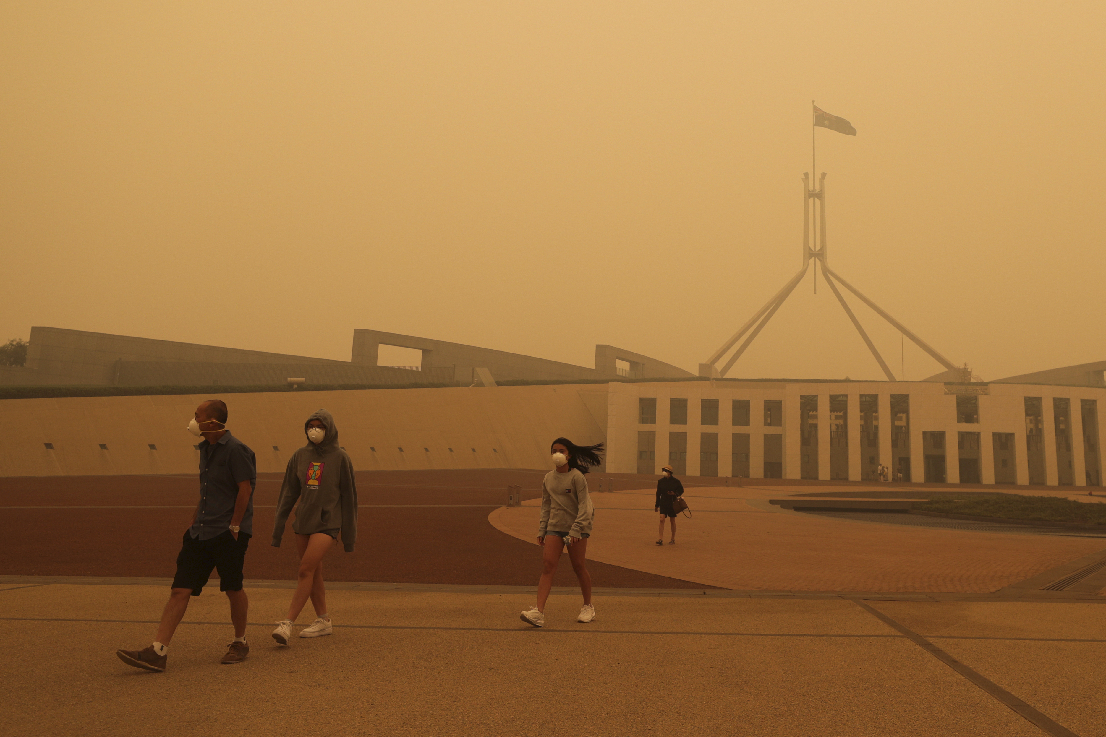 Four people walking outside an Australian museum in haze and smoke with masks on