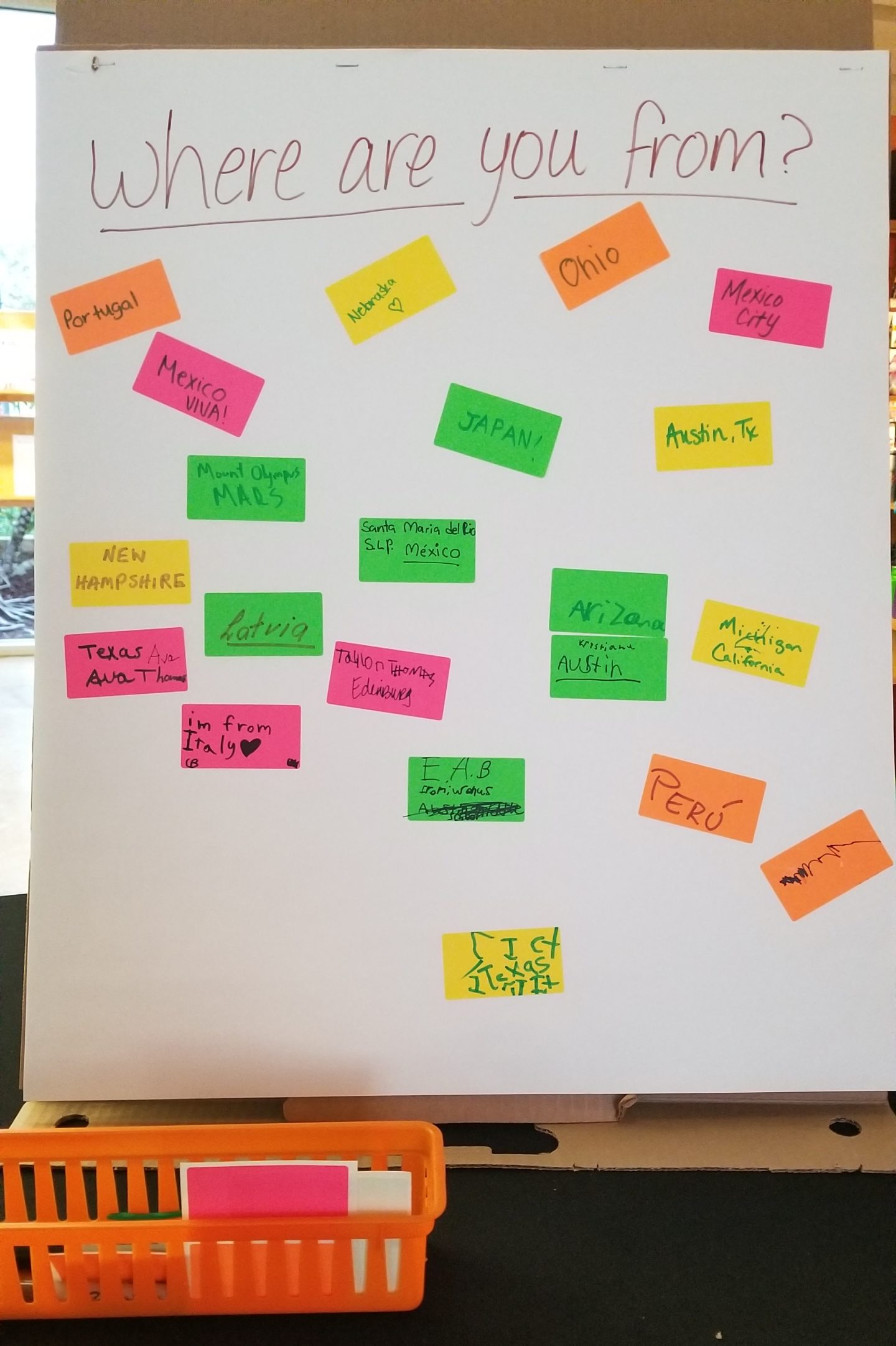 A large sheet of paper with "Where are you from?" written at the top, with colorful sticky notes below that say answers like "Portugal," 'Nebraska," "Ohio," "Mexico City," "Mexico / VIVA!," "JAPAN!," and "Austin, Tx."
