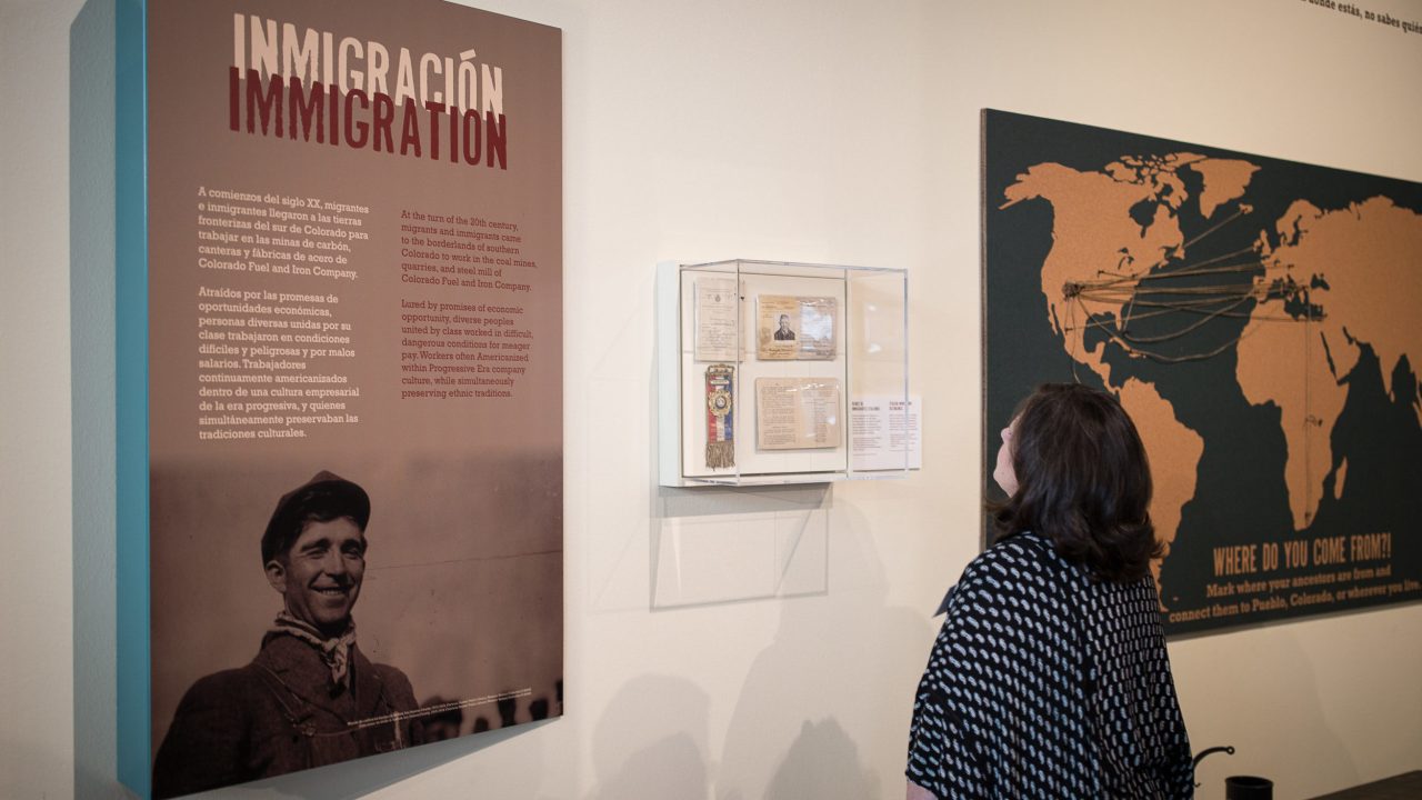 A visitor in a gallery reading a placard that says "Immigration" in English and Spanish.