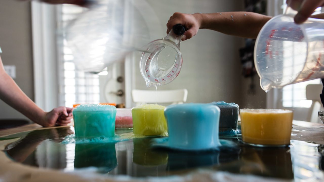 Children pouring water into beakers of colorful liquid
