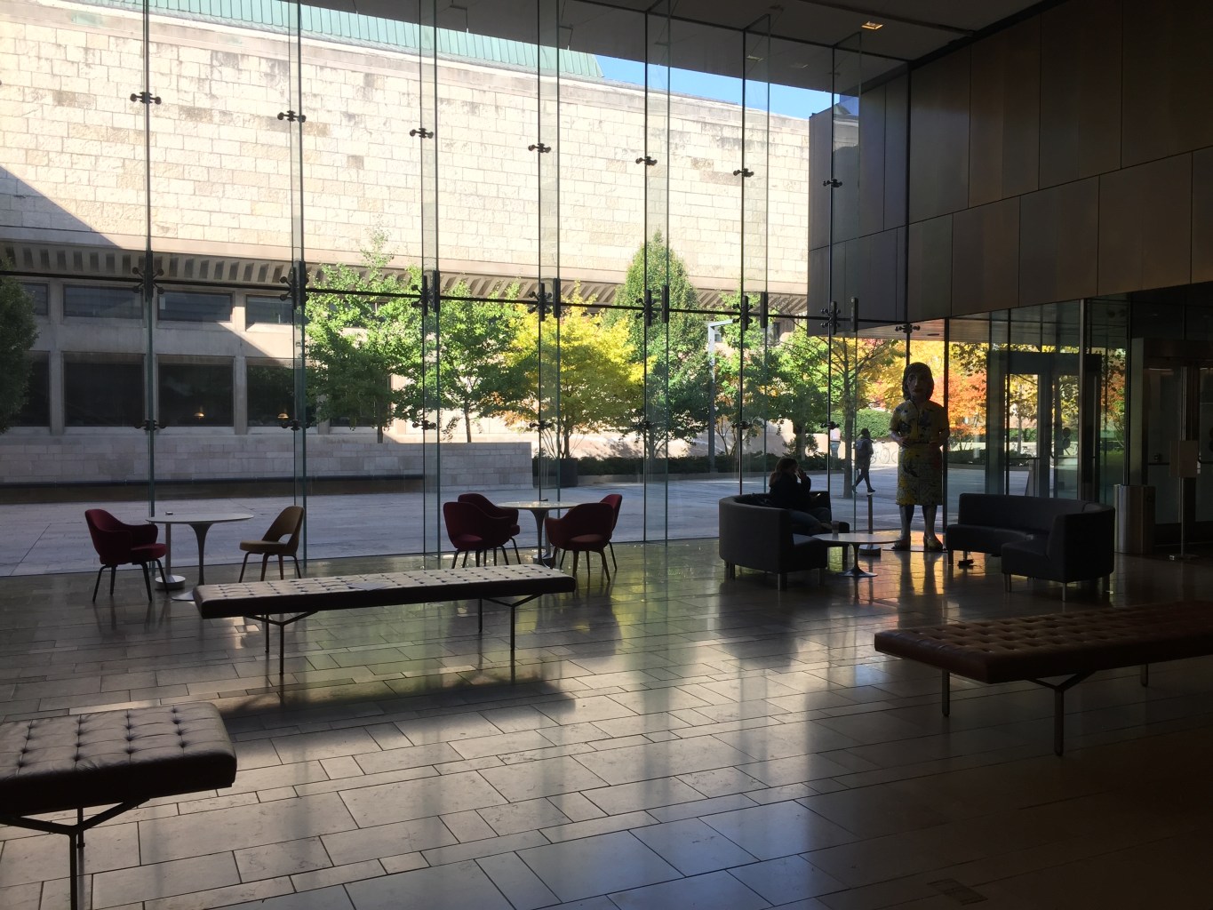 A lobby space with floor-to-ceiling glass walls and cafe-style tables and benches.