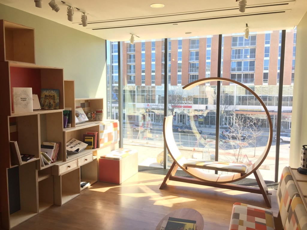 A round wood chair and modular shelves next to a floor-to-ceiling glass window