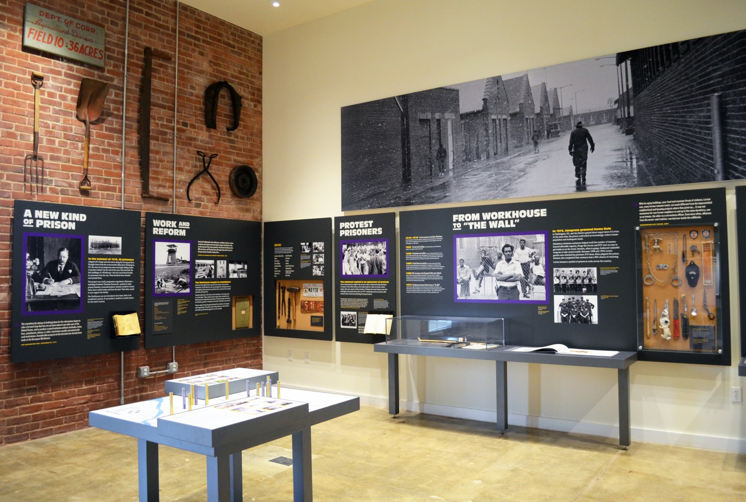 Work implements and restraints are mounted to a display wall, above panels describing the prison's history as a progressive reformatory.