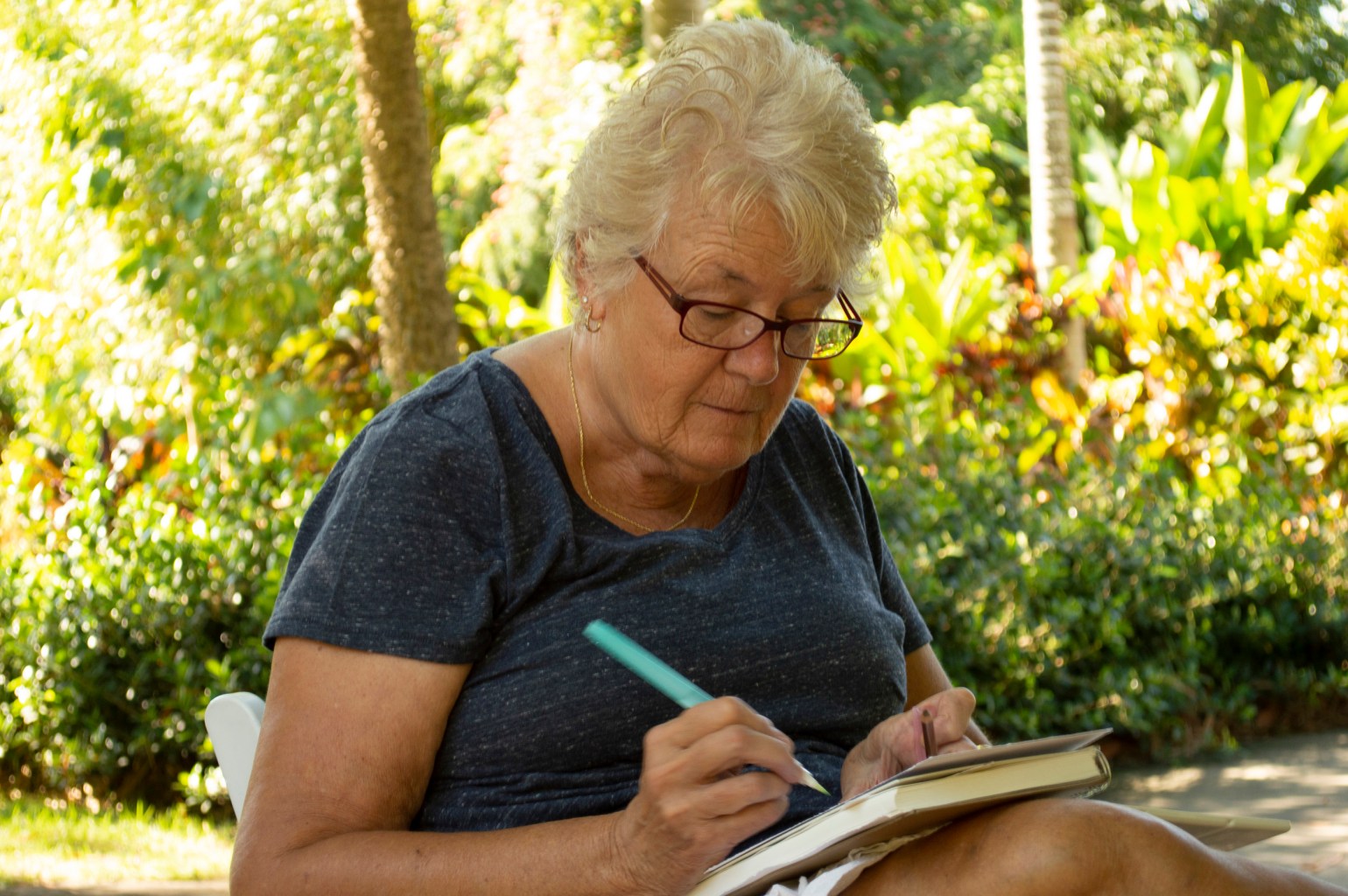 A person in a garden concentrating on a piece of paper with a drawing implement in hand