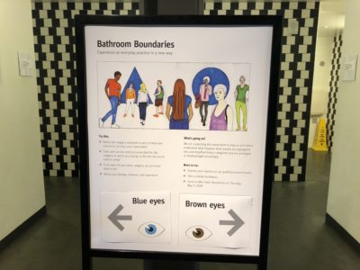 A bathroom sign showing various types of people and suggestions for which bathroom to use suggesting that blue eyed people go to the left and brown eyed people go to the right. 