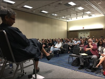 Interior of a crowded conference room and a presenter sitting on stage