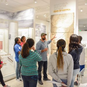 A gallery tour with a Global Guide speaking and gesticulating toward a graphic on display.