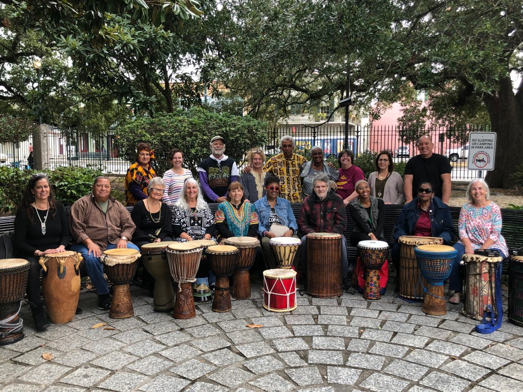 Participants posing for a large group portrait in front of standing drums