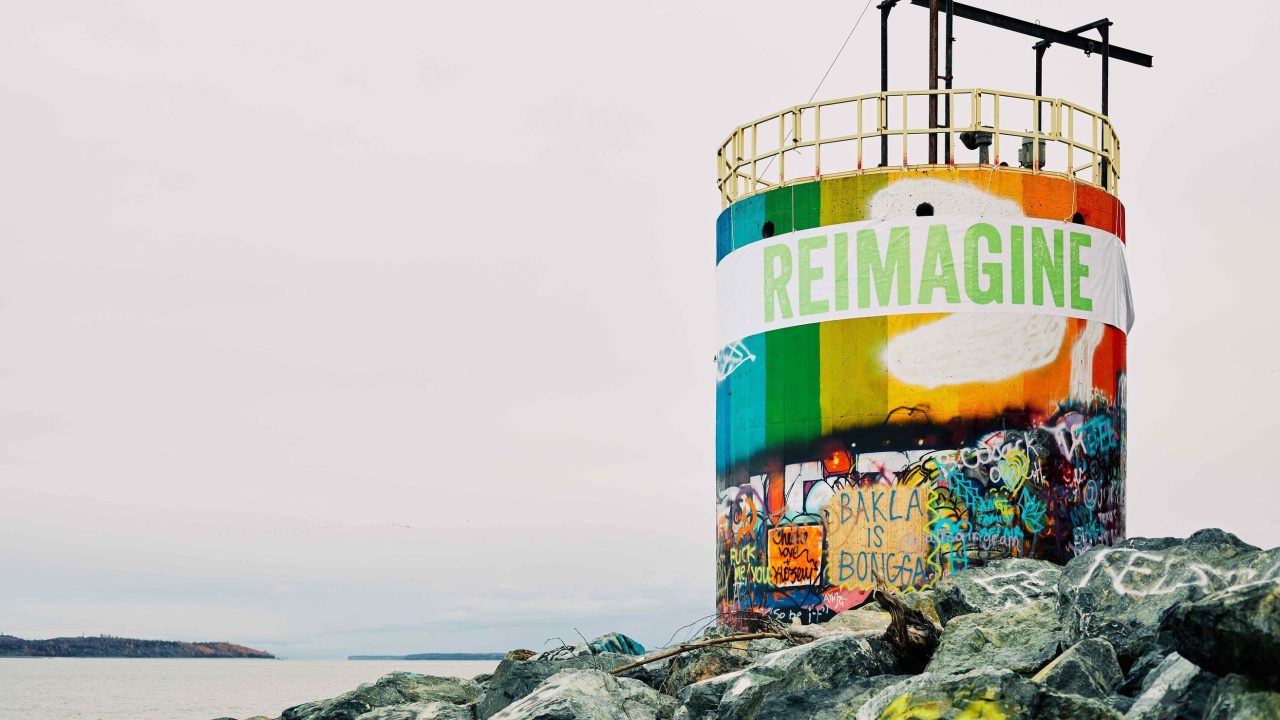 A water tower with a mural drawn on it reading "Reimagine"