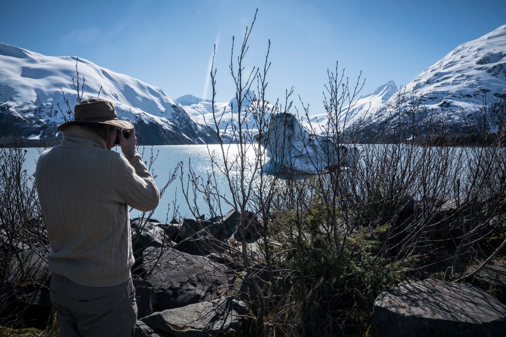 A person holds a camera out toward a glacier floating in a river