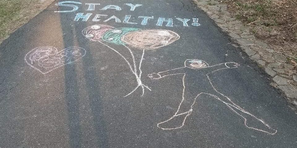 Sidewalk chalk graffiti reading "Stay Healthy!" with a drawing of a person holding a bundle of balloons
