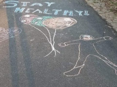 Sidewalk chalk graffiti reading "Stay Healthy!" with a drawing of a person holding a bundle of balloons
