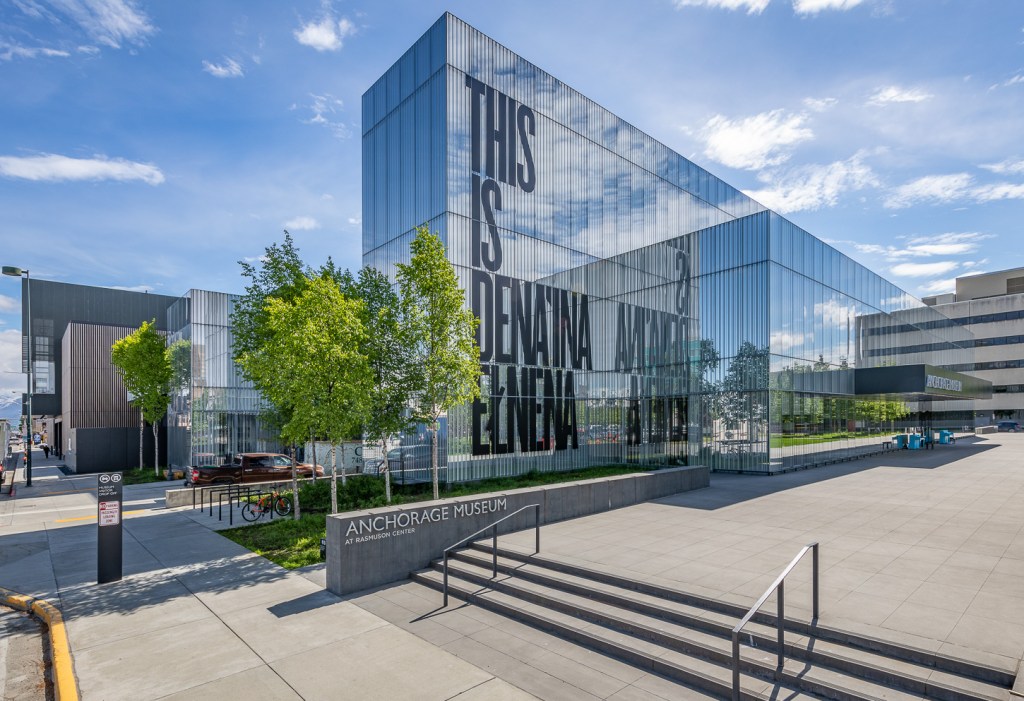 A glass building facade with large letters reading "This is Dena'ina Elnena"