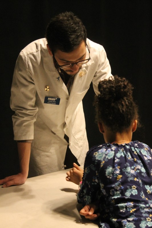 An educator wearing a lab coat standing with a young student