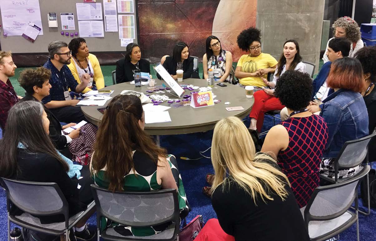 A group of individuals sit around a round table in discussion.