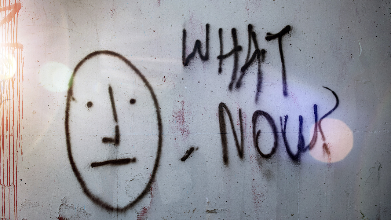Graffiti reading "What Now" with a drawing of an uncertain face.