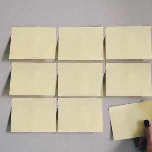 A grid of sticky notes on a wall with a hand reaching up to place one