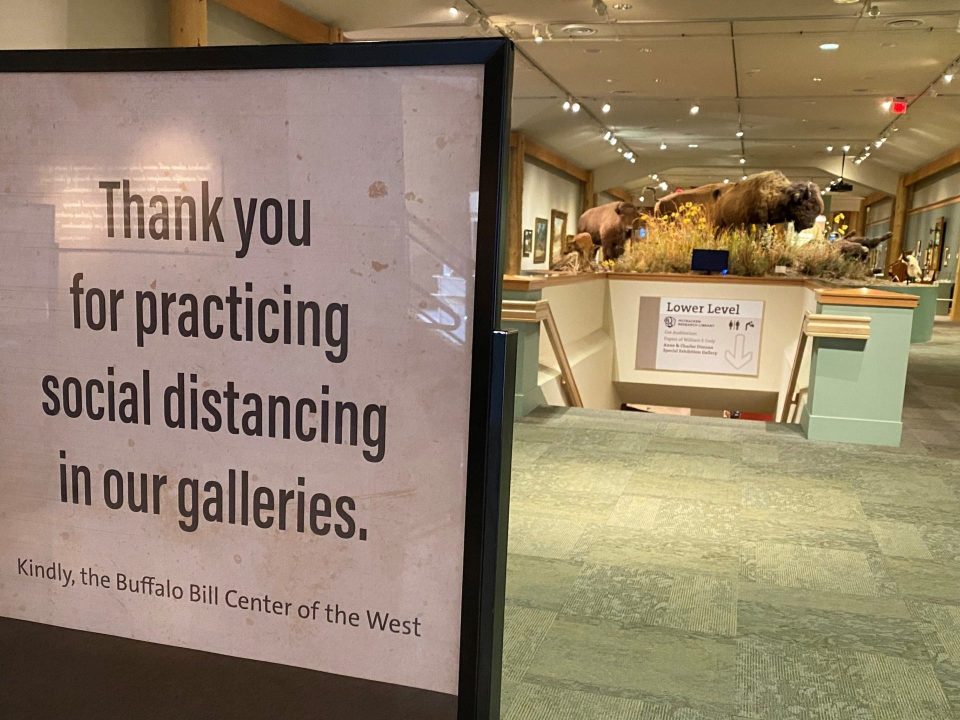 Inside of a museum lobby, a sign reading, "Thank you for practicing social distancing in our galleries. Kindly, Buffalo Bill Center of the West.
