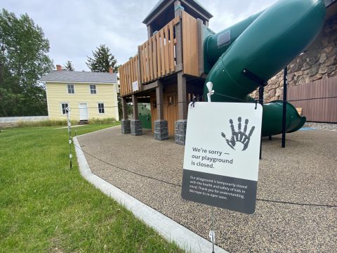 A sign in front of an outdoor playground reading, "We're sorry—our playground is closed. Our playground is temporarily closed with the health and safety of kids in mind. Thank you for understanding. We hope to re-open soon.