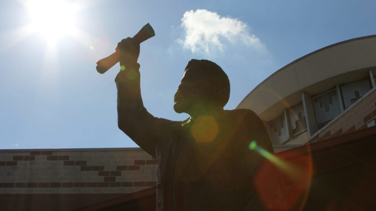 Sculpture of a man holding up paper scroll in his fist