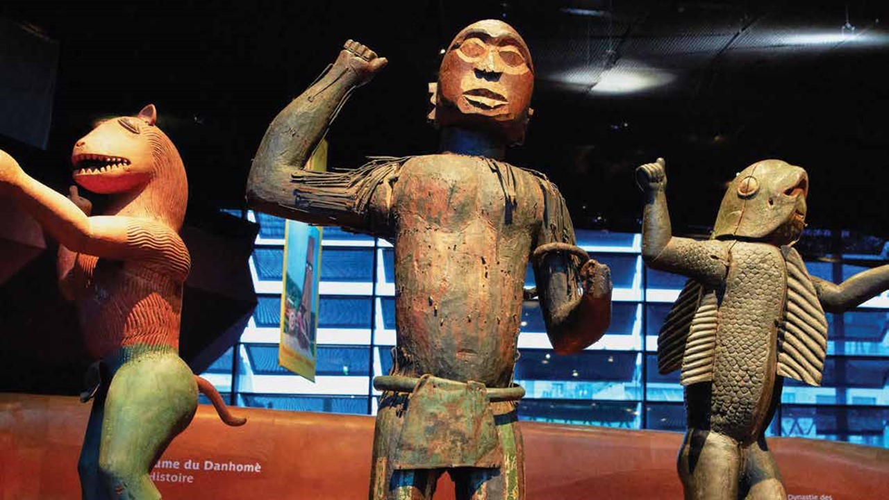 Three Benin bronze statues stand in a museum exhibition.