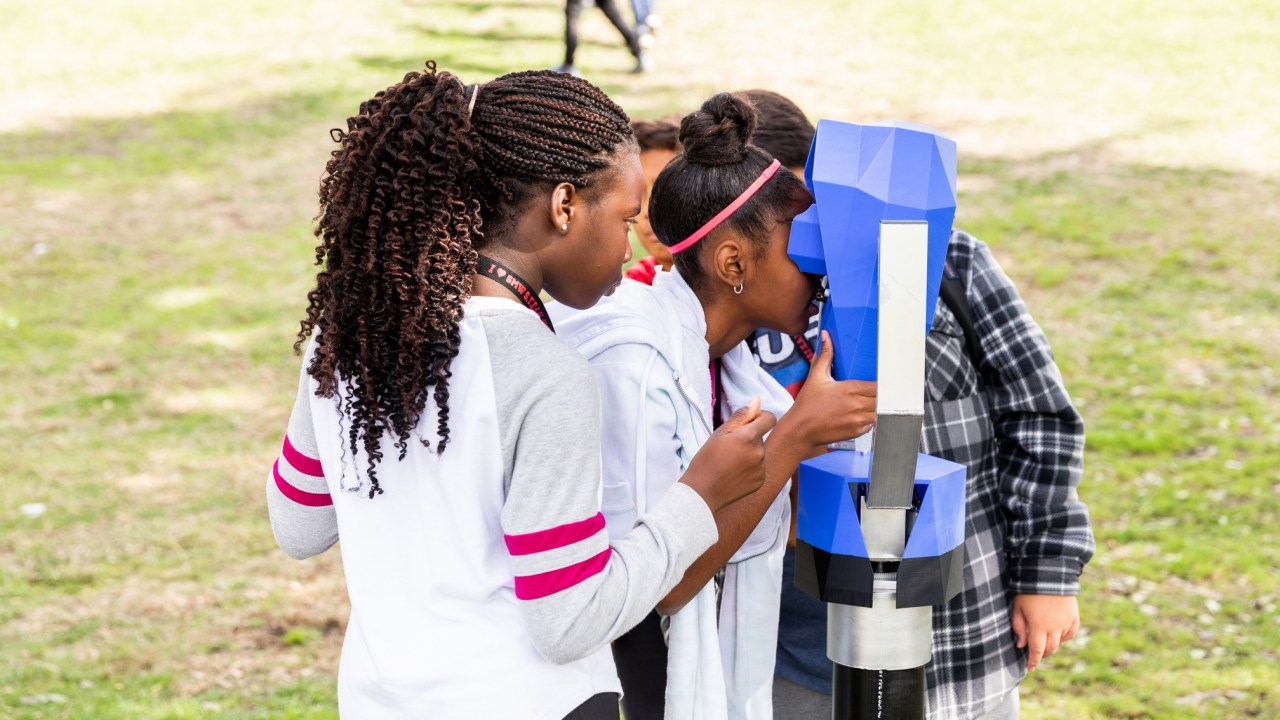 Children looking into a blue device resembling a periscope