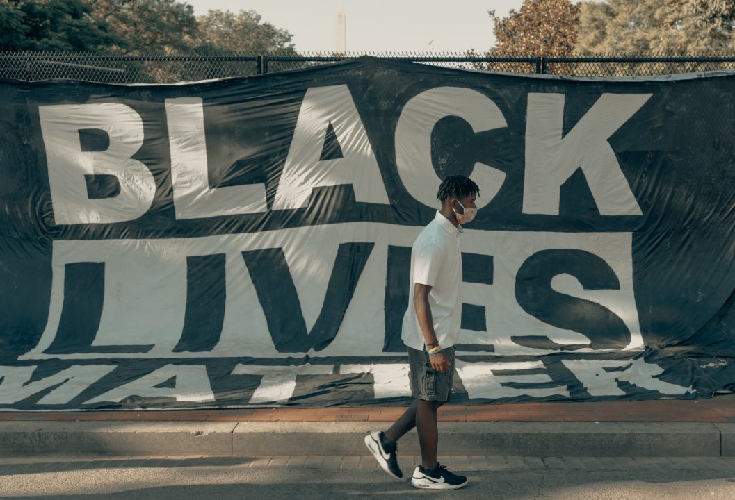 A teenager wearing a face mask walking past a Black Lives Matter banner hung on a fence
