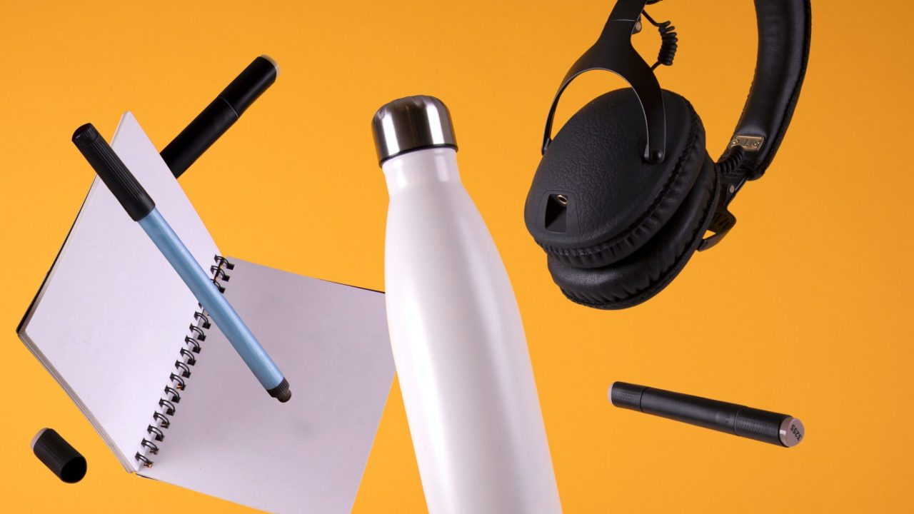 An array of study tools, including a notebook, water bottle, and headphones, against a yellow background.