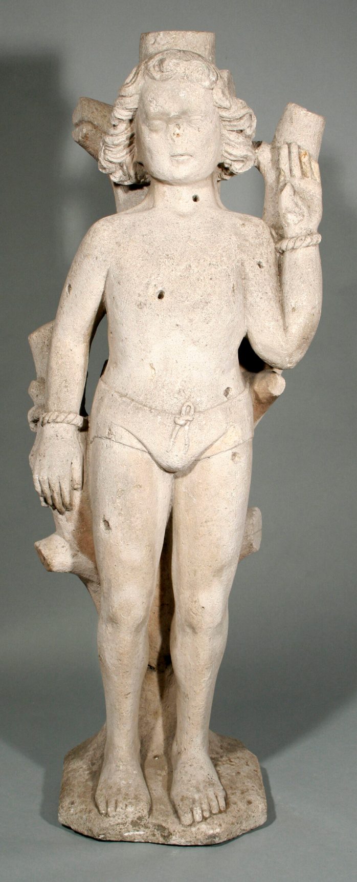 A limestone statue of a child-sized figure with holes visible all over the body