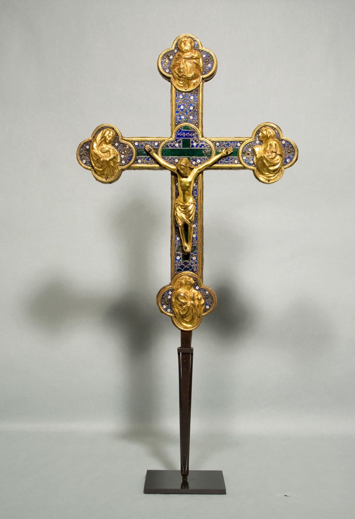An ornate crucifix made of gold, enamel, and other materials on a long base
