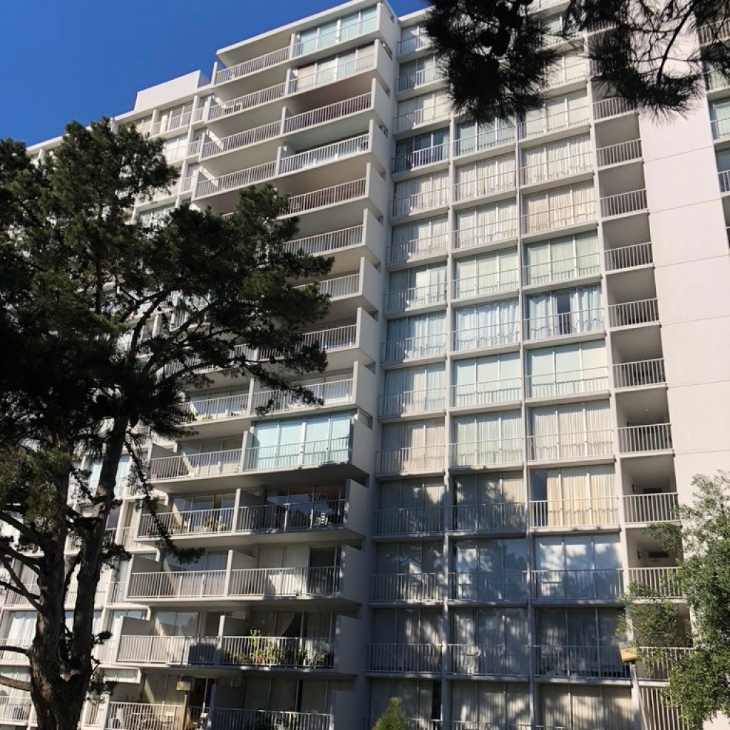 A tall, modernist apartment building with white curtains visible in the windows