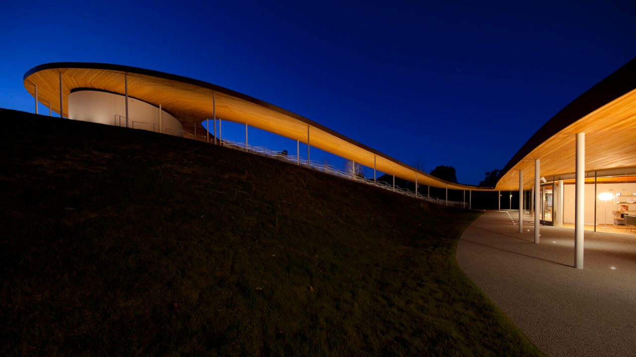 A contemporary building whose facade extends into a large outdoor wooden pavilion.