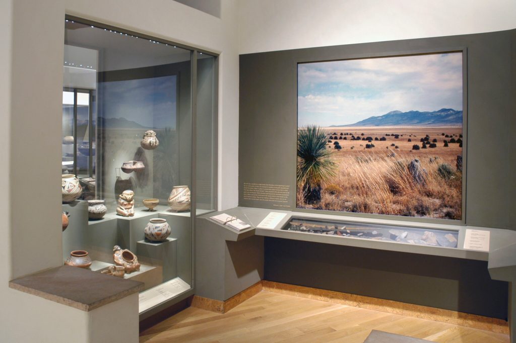 An exhibition gallery of pottery and a photograph of a desert landscape