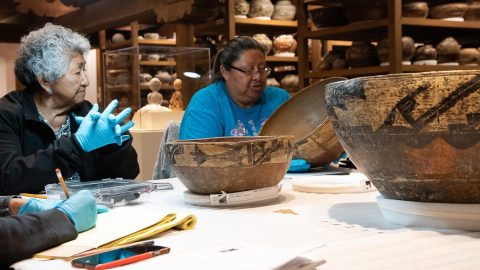 People sitting around a table wearing gloves and looking at Native pottery