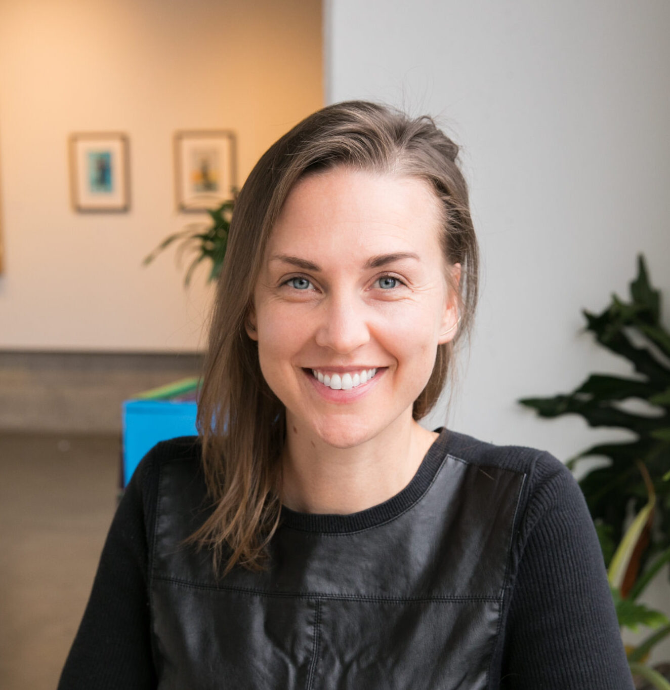 Headshot of Dana P. Hundley, sitting in an office in front of a plant and paintings on the walls