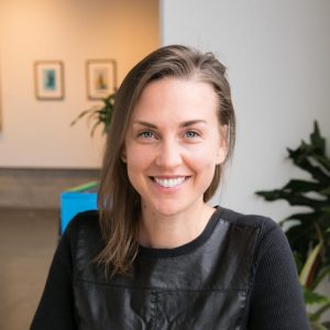 Headshot of Dana P. Hundley, sitting in an office in front of a plant and paintings on the walls