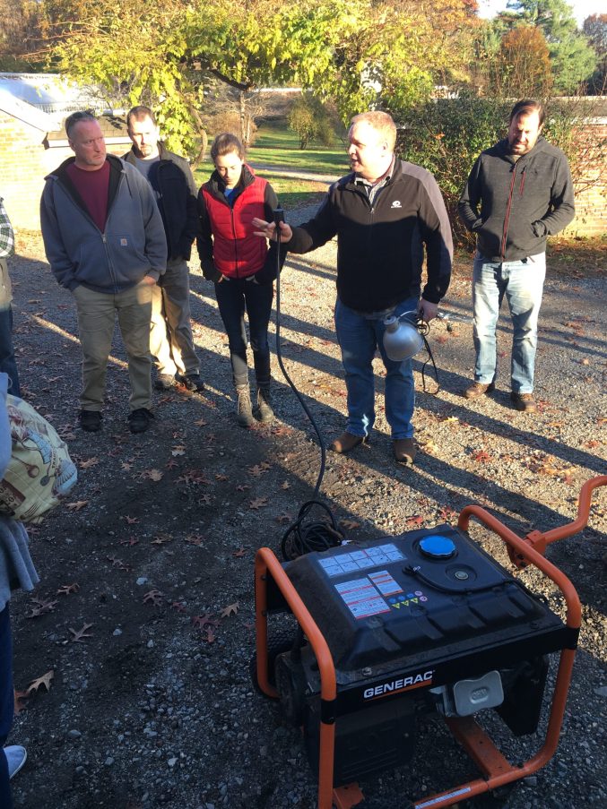 A group of people outdoors standing around a power generator