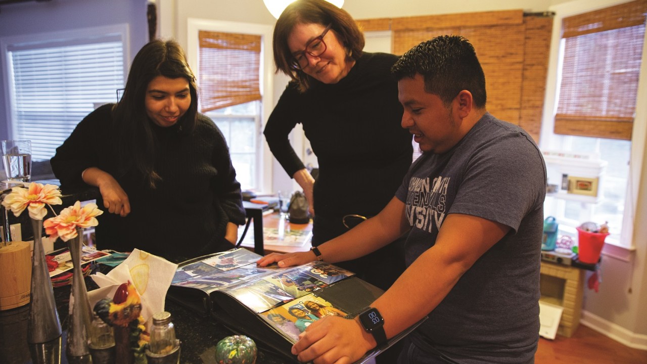Three people stand looking at a scrapbook.