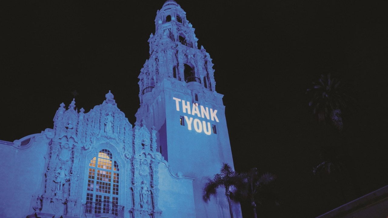 An exterior shot of the Museum of Us with "Thank You" projected onto the facade.