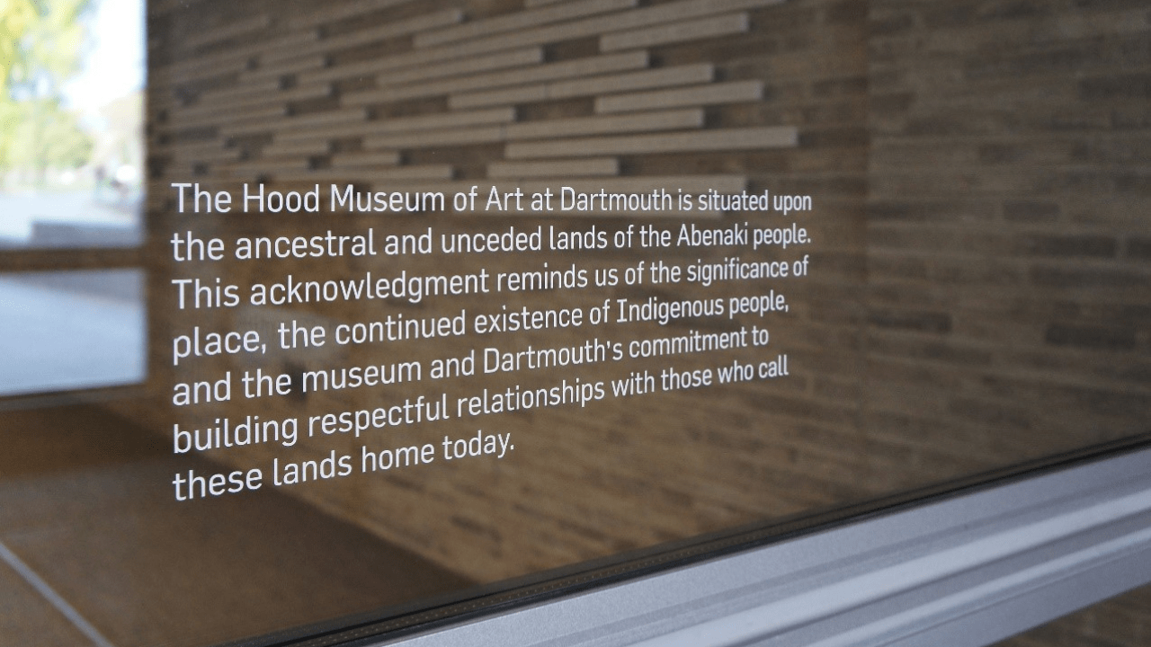 A decal on a window reading "The Hood Museum of Art at Dartmouth is situated upon the ancestral and unceded lands of the Abenaki people. This acknowledgment reminds us of the significance of place, the continued existence of Indigenous people, and the museum and Dartmouth's commitment to building respectful relationships with those who call these lands home today."