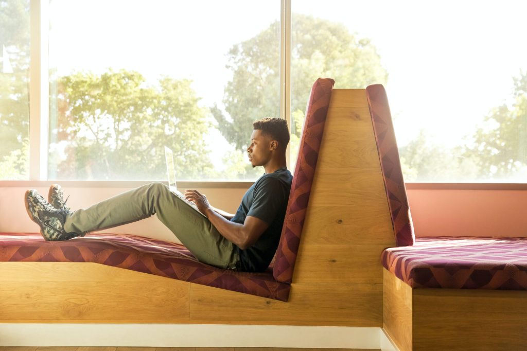 A person sitting in a modern ramp-like seating area while working on a laptop