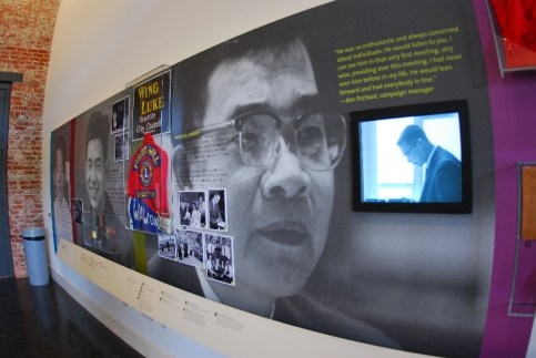 A gallery wall at a museum showing a video, photos, and ephemera