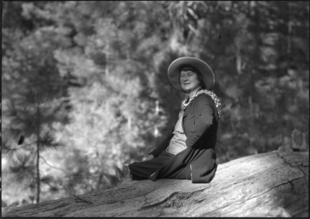 Black-and-white photo of a subject sitting on an overturned tree stump in a forest