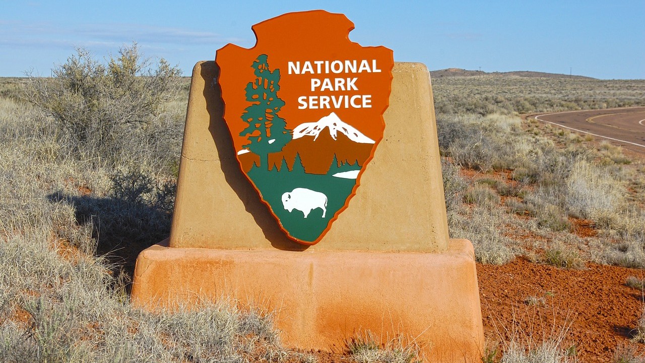 A sign with the National Park Service logo on it, in from of a desert landscape