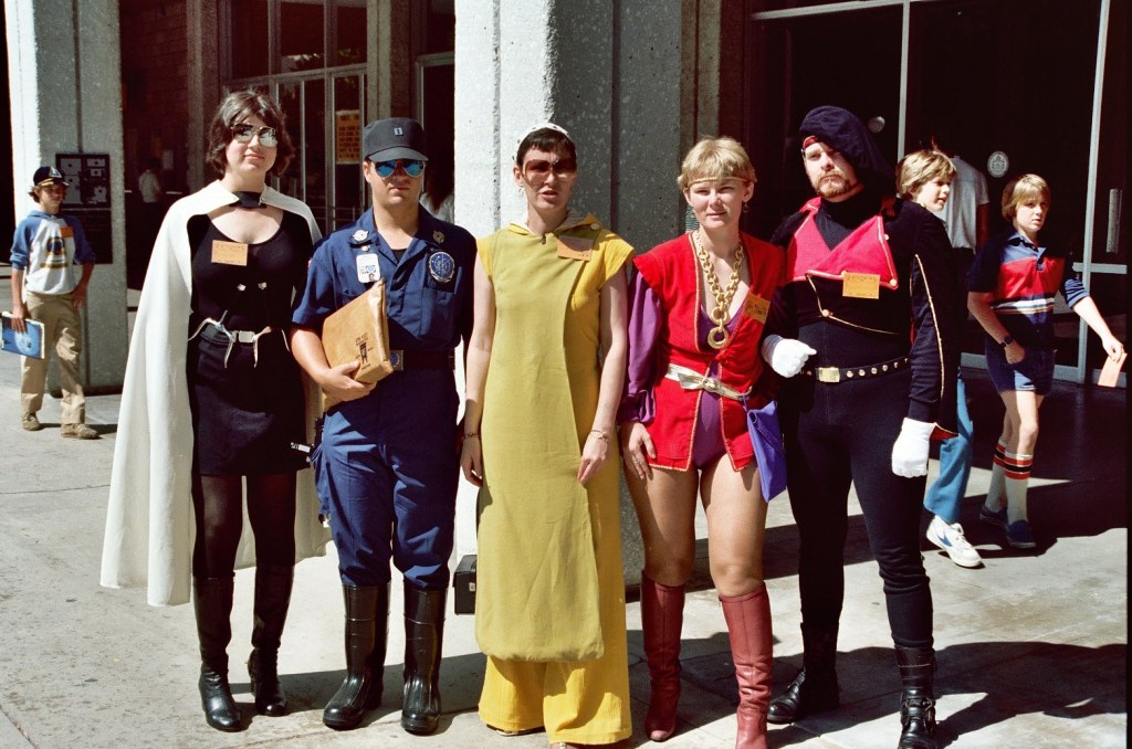 A group of people wearing a variety of costumes outside of a convention center