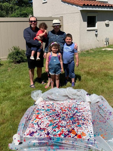A family with children standing in front of a canvas on a lawn covered in splattered paint