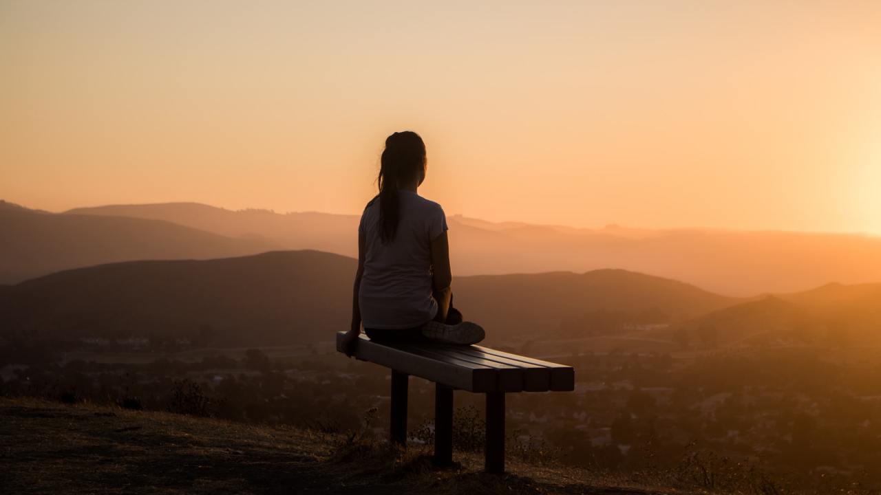 A person sitting on a bench looking down at mountains at sunset