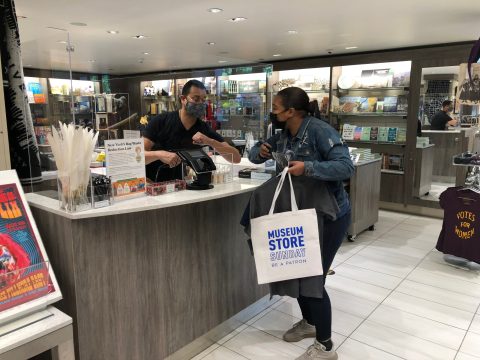 A museum store employee and patron elbow-bumping at the cash register