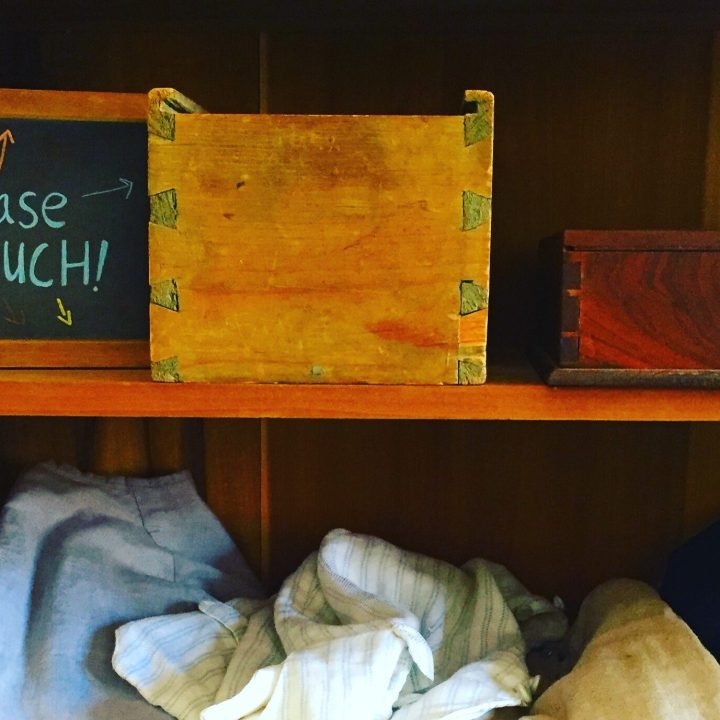 A shelf with period costumes and objects displayed with a chalkboard sign reading "Please Touch!"
